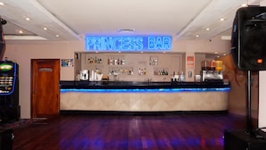 Een bar genaamd "Princess Bar" met een neonbord, een toonbank met verschillende flessen en een houten vloer.