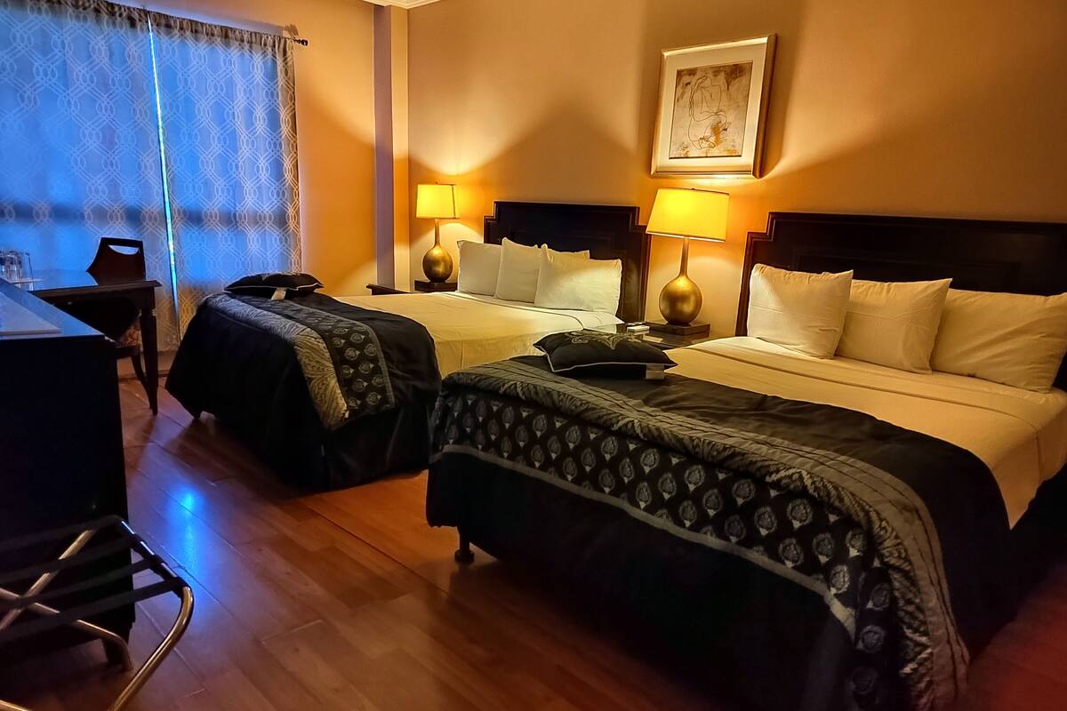 Hotelkamer met twee bedden, een bureau en een stoel. Er staan lampen aan weerszijden van de bedden en er hangt een schilderij aan de muur.
