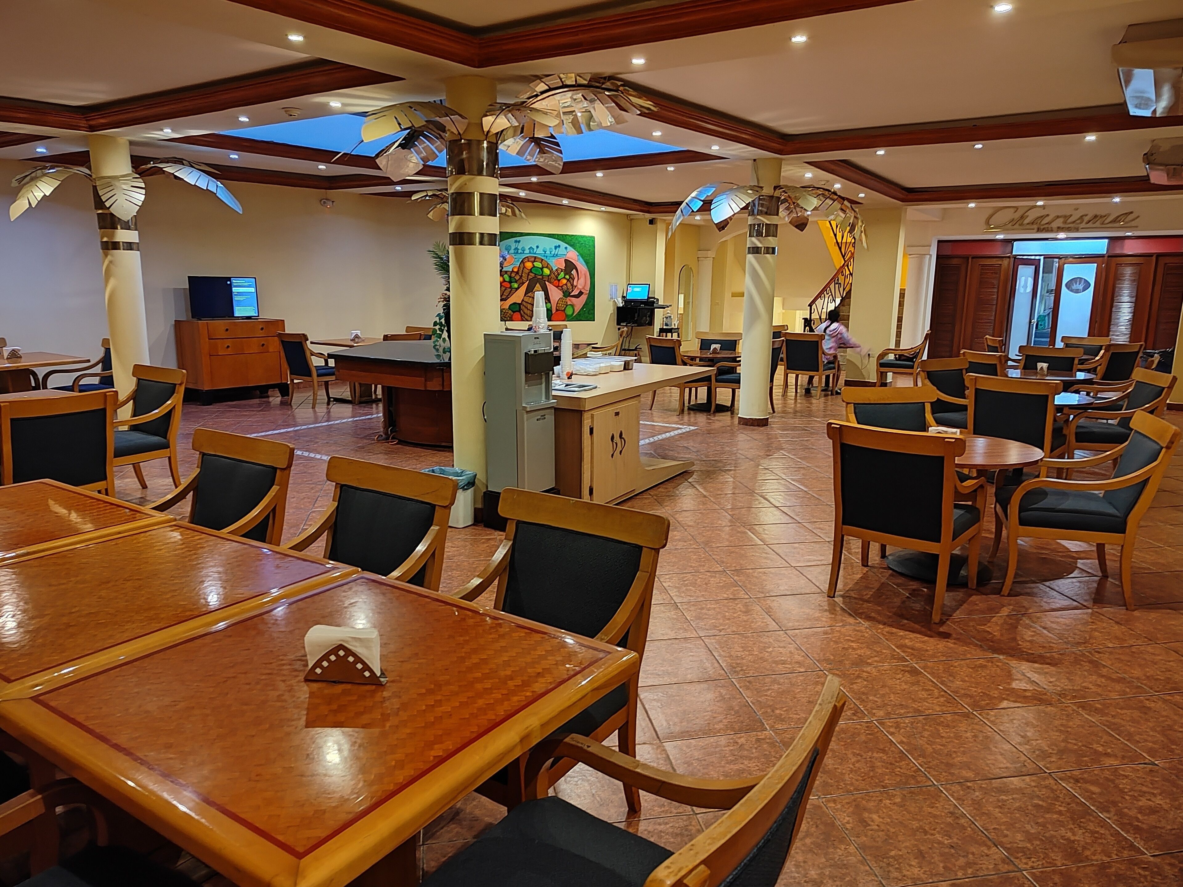 Un restaurante espacioso con mesas y sillas de madera, una barra central y elementos decorativos en el techo.