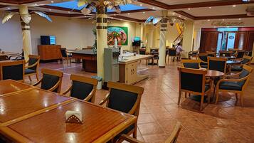 Un restaurante espacioso con mesas y sillas de madera, una barra central y elementos decorativos en el techo.