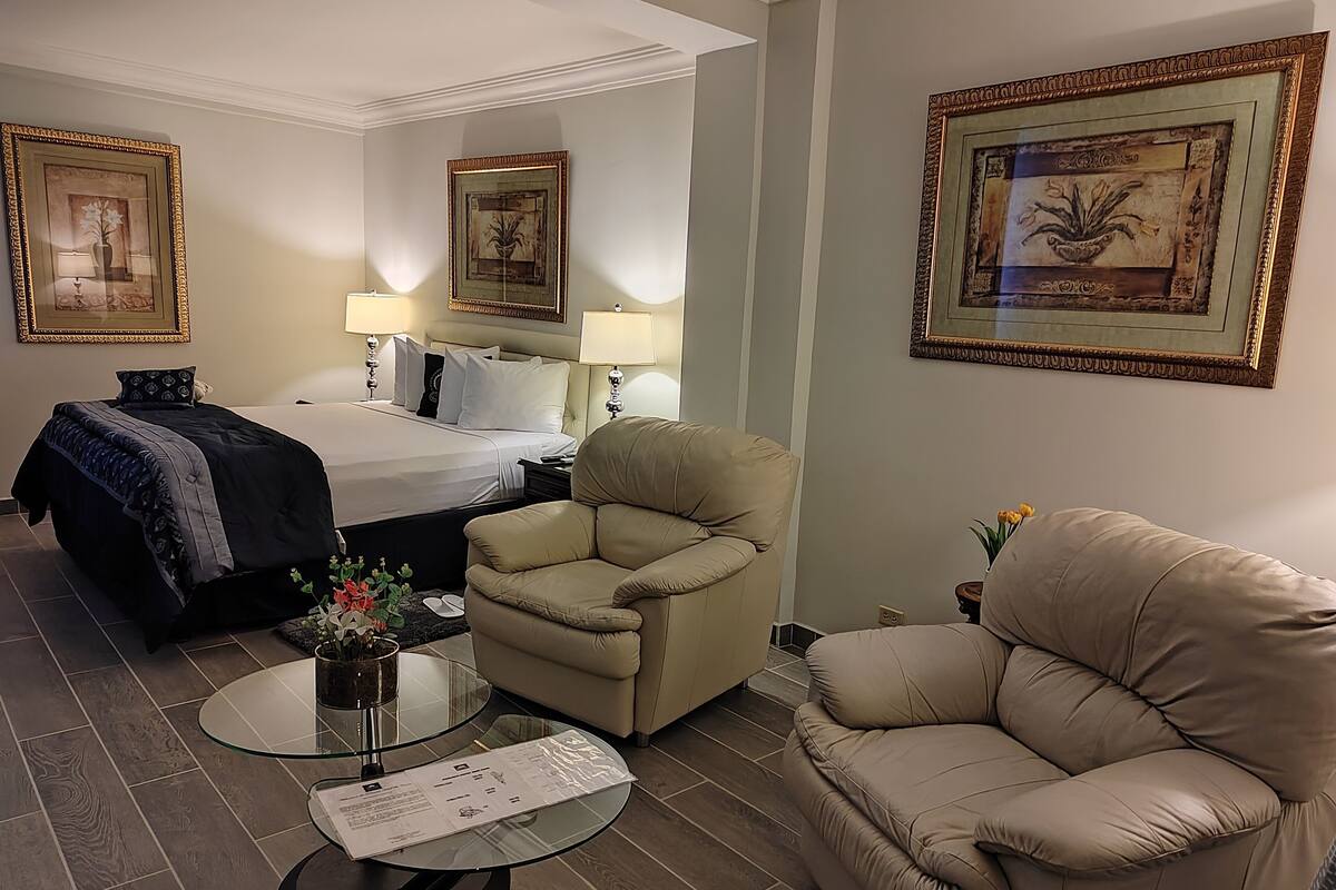 Een hotelkamer met een bed, twee stoelen, een glazen salontafel en een bijzettafeltje met een bloevas.