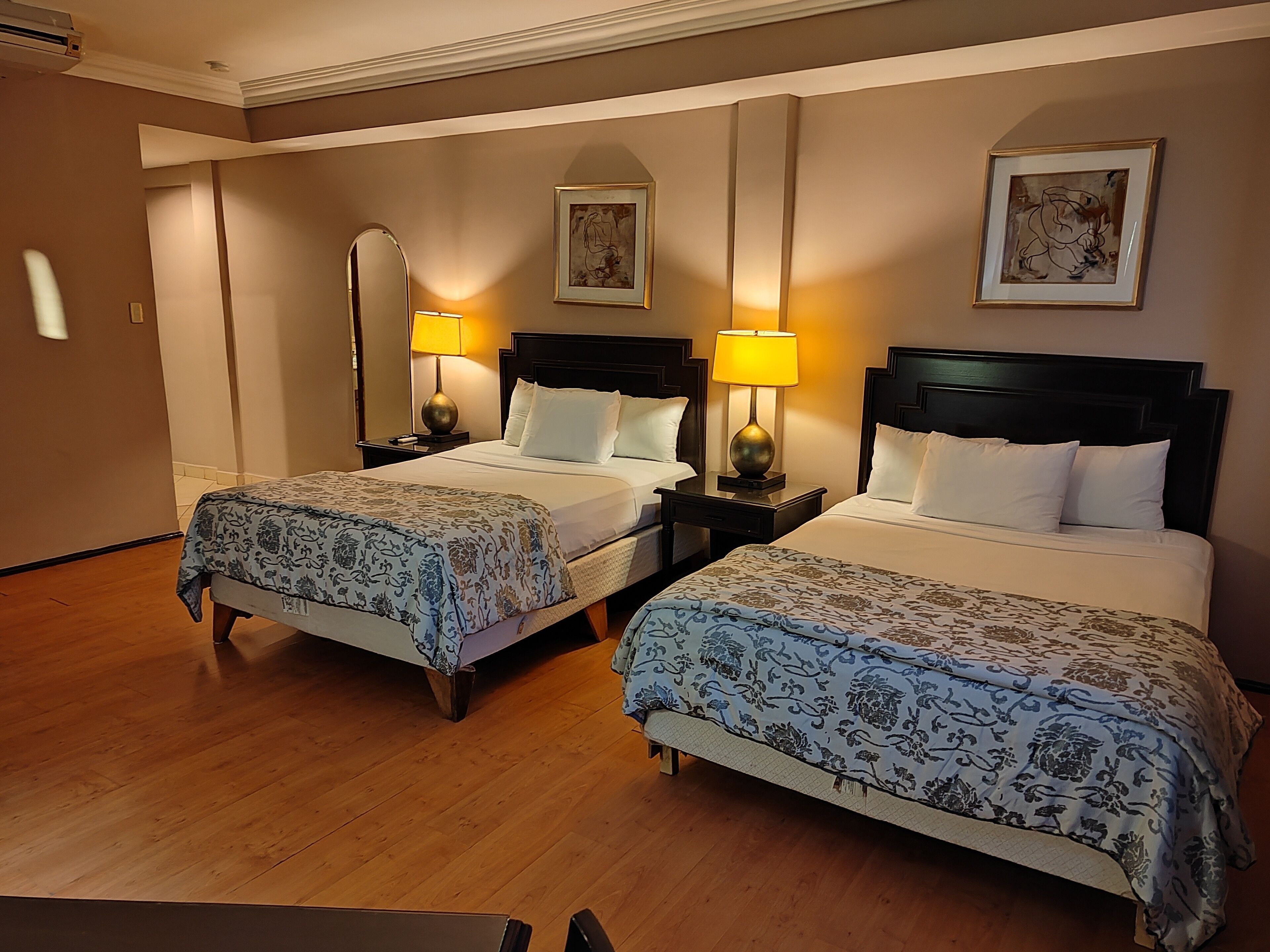 A hotel room with two beds, each with a headboard, bedside tables, lamps, and floral-patterned bedspreads.