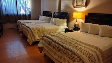 Habitación de hotel con tres camas, piso de madera, una mesita de noche con lámpara y un cuadro enmarcado en la pared.