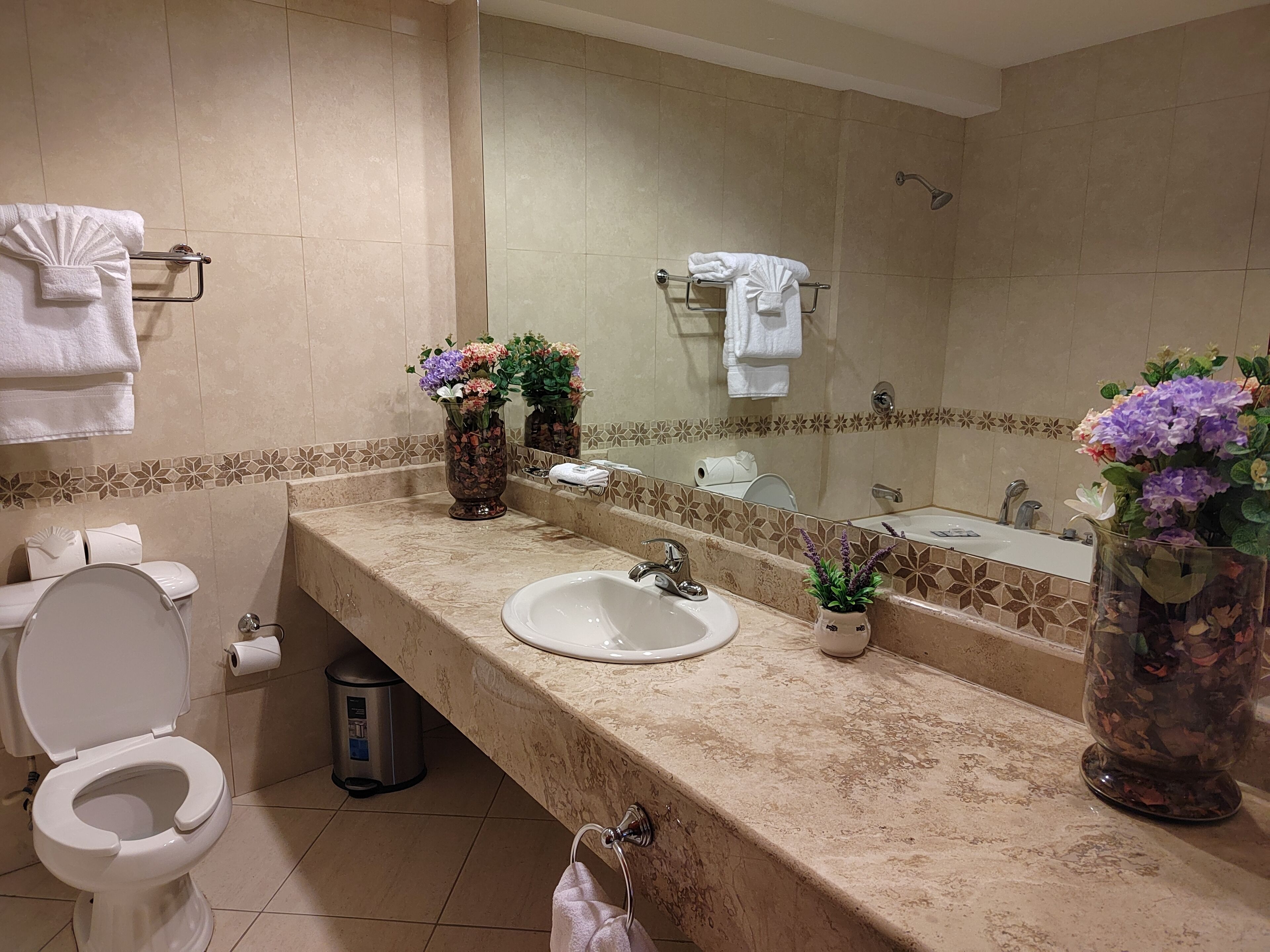 A bathroom with a toilet, sink, and shower. There are towels hanging on a rack and flowers in vases on the counter.