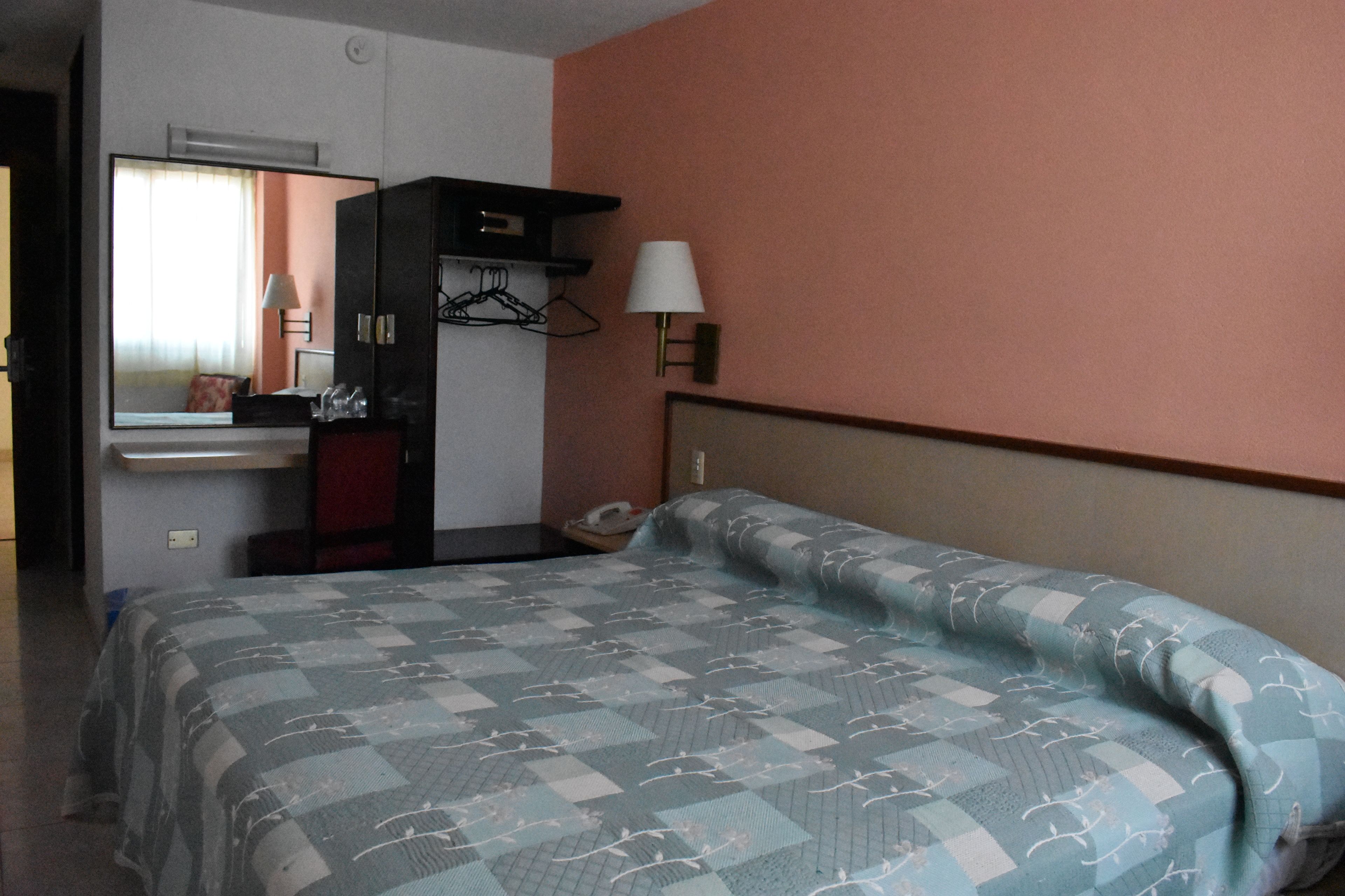 Une chambre d’hôtel équipée d’un lit, d’un bureau, d’un miroir et d’une lampe fixée au mur.
