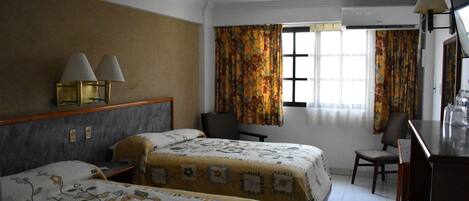 A hotel room with two beds, a desk, a chair, and a window with curtains.