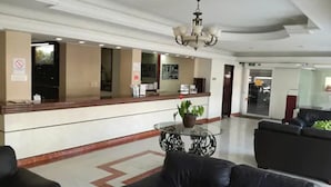 A hotel lobby with a reception desk, a chandelier, a round table with a plant, and black leather sofas.