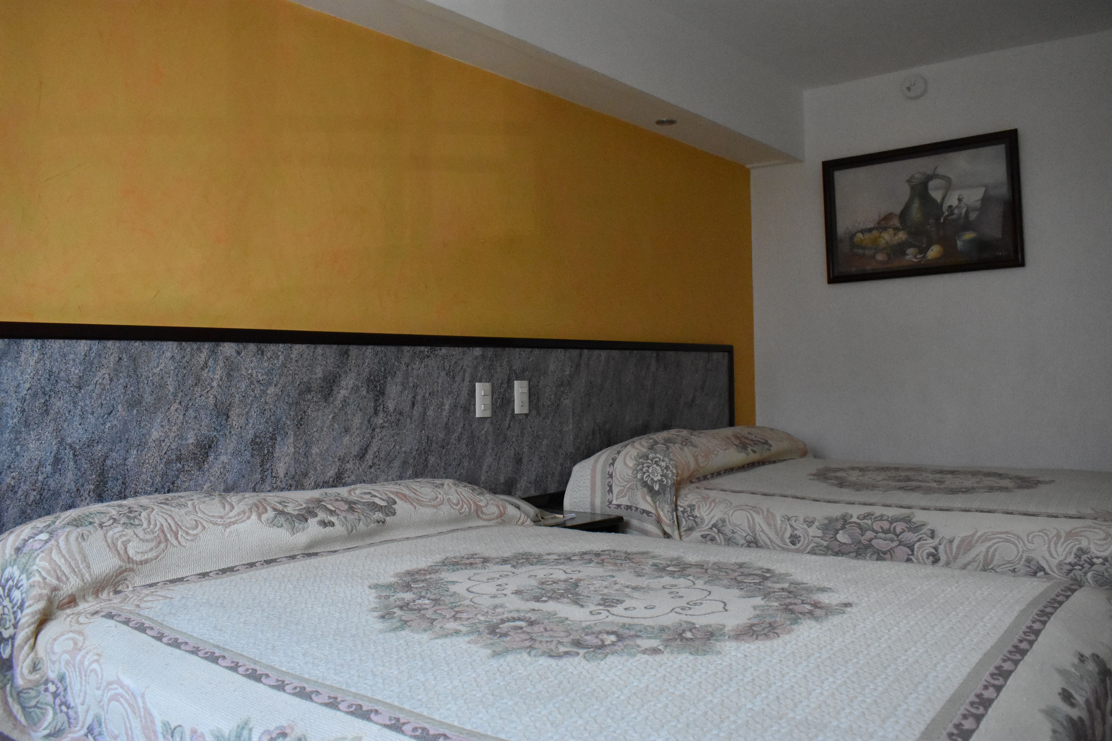 A bedroom with two beds, a marble headboard, and a painting on the wall.