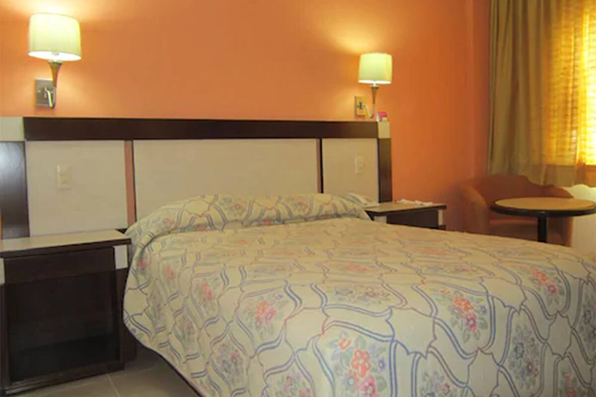 Quarto de hotel com uma cama grande, duas mesas de cabeceira, uma cadeira e uma pequena mesa.