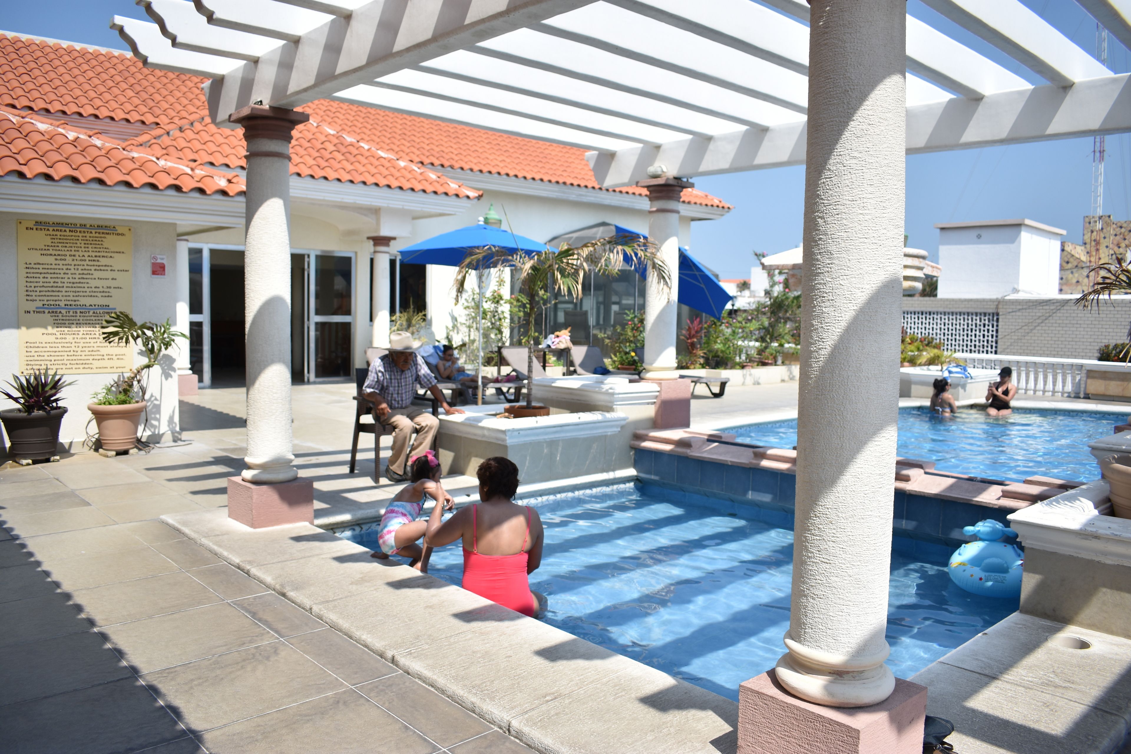 Zona de piscina con terraza cubierta, columnas y plantas en macetas.