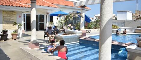 Zona de piscina con terraza cubierta, columnas y plantas en macetas.
