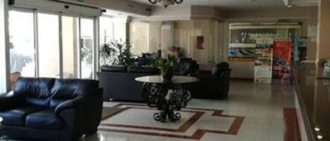 Un vestíbulo de hotel con una recepción, un sofá de cuero negro, una araña y un piso de baldosas.