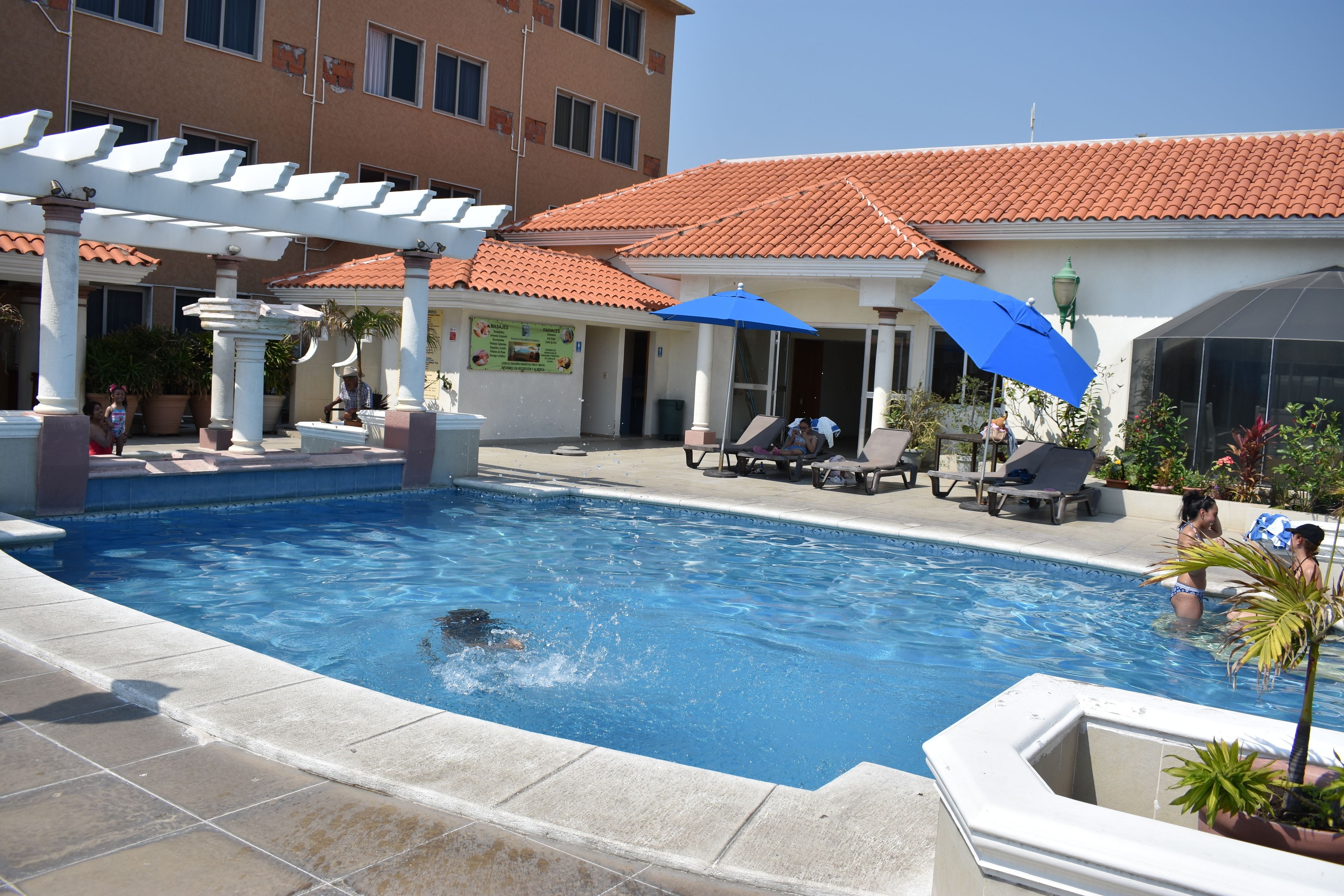 A swimming pool with a white pergola, lounge chairs, and umbrellas.