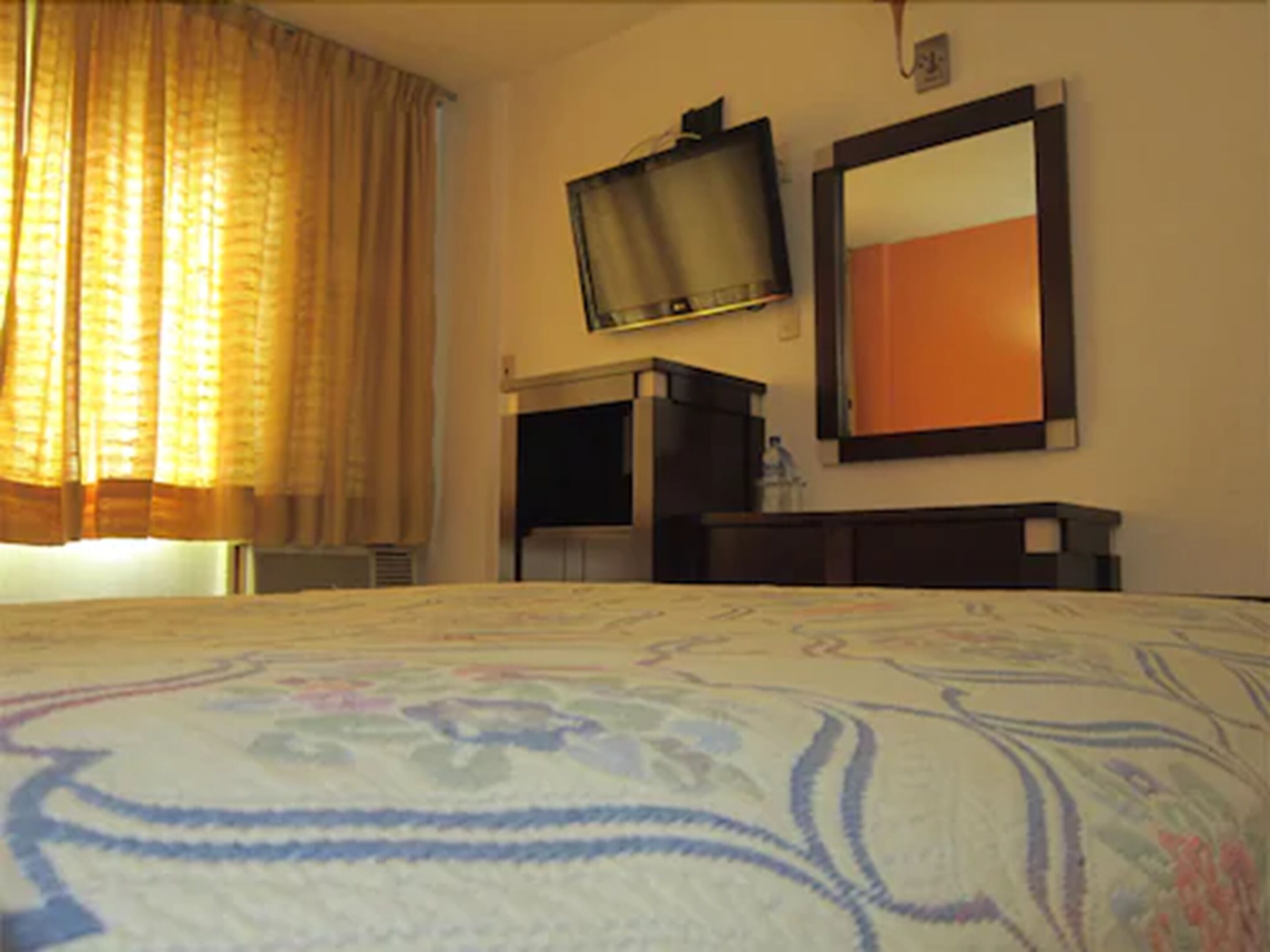 A hotel room with a bed, a television mounted on the wall, and a mirror.
