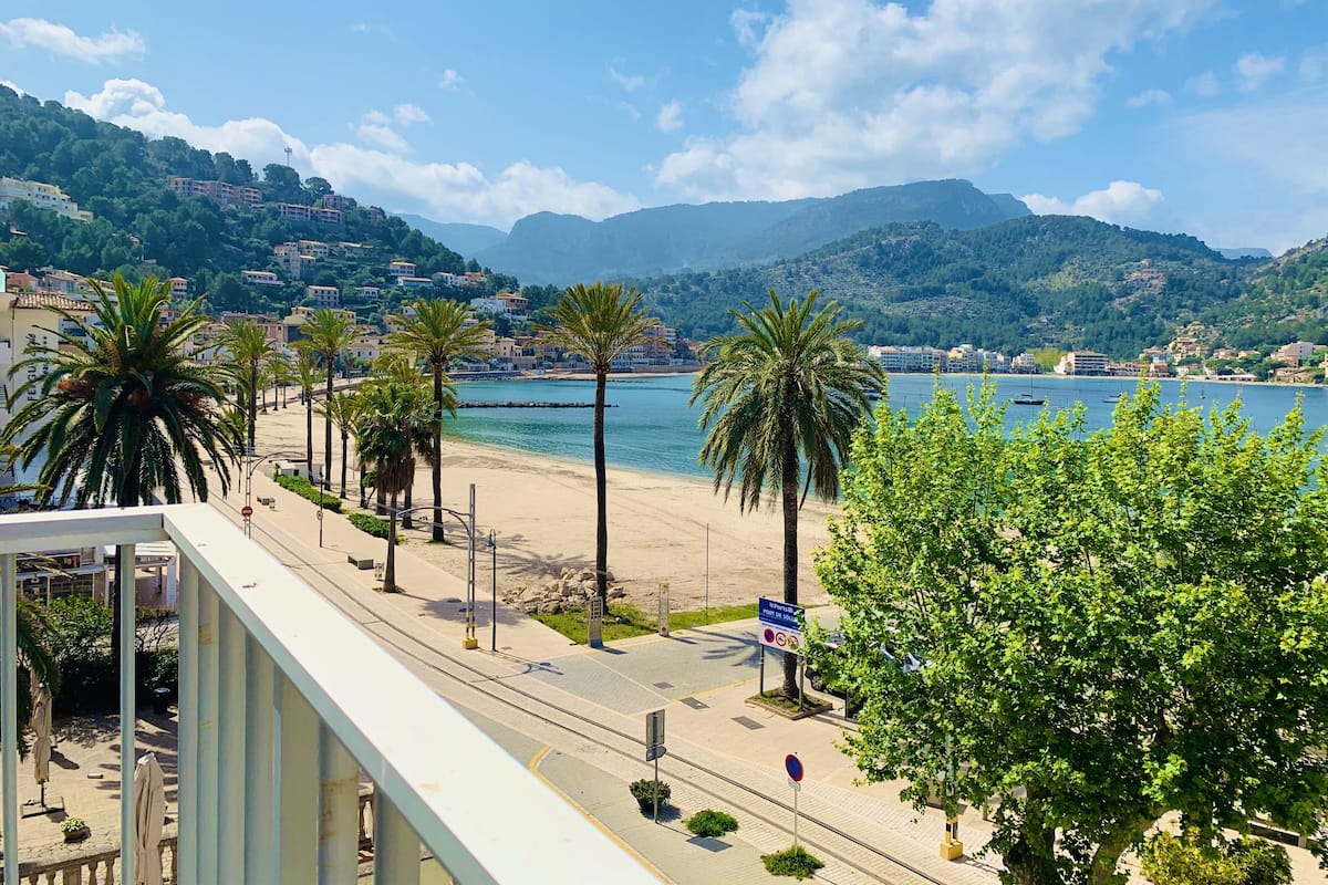 Una carretera costera con palmeras, una playa y edificios al fondo.