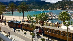 Un poble costaner amb un tramvia, palmeres i embarcacions al port.