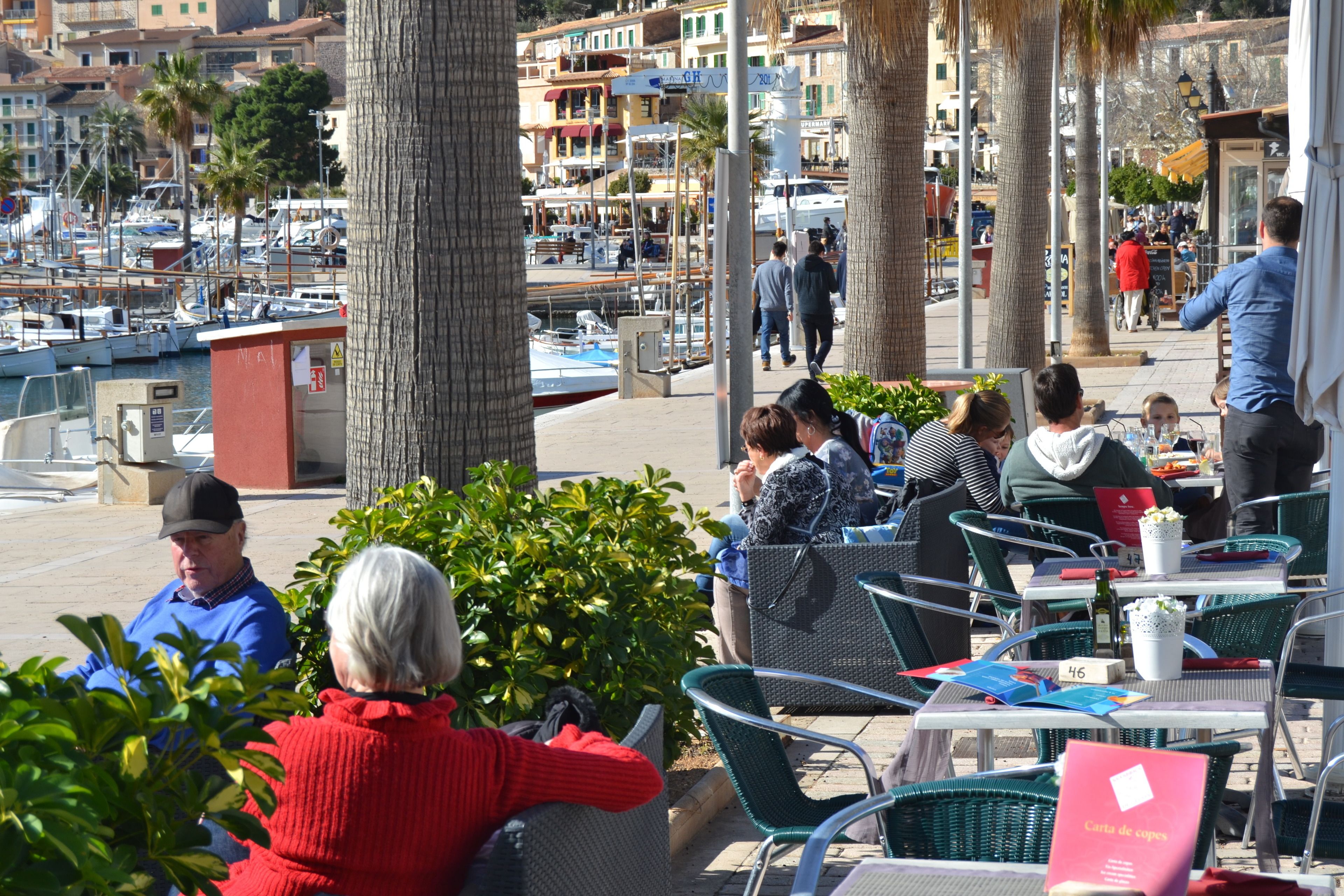 An outdoor cafe with tables and chairs, overlooking a marina with boats.
