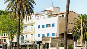 Un edifici de diversos pisos amb balcons, palmeres i un sòl de sorra.