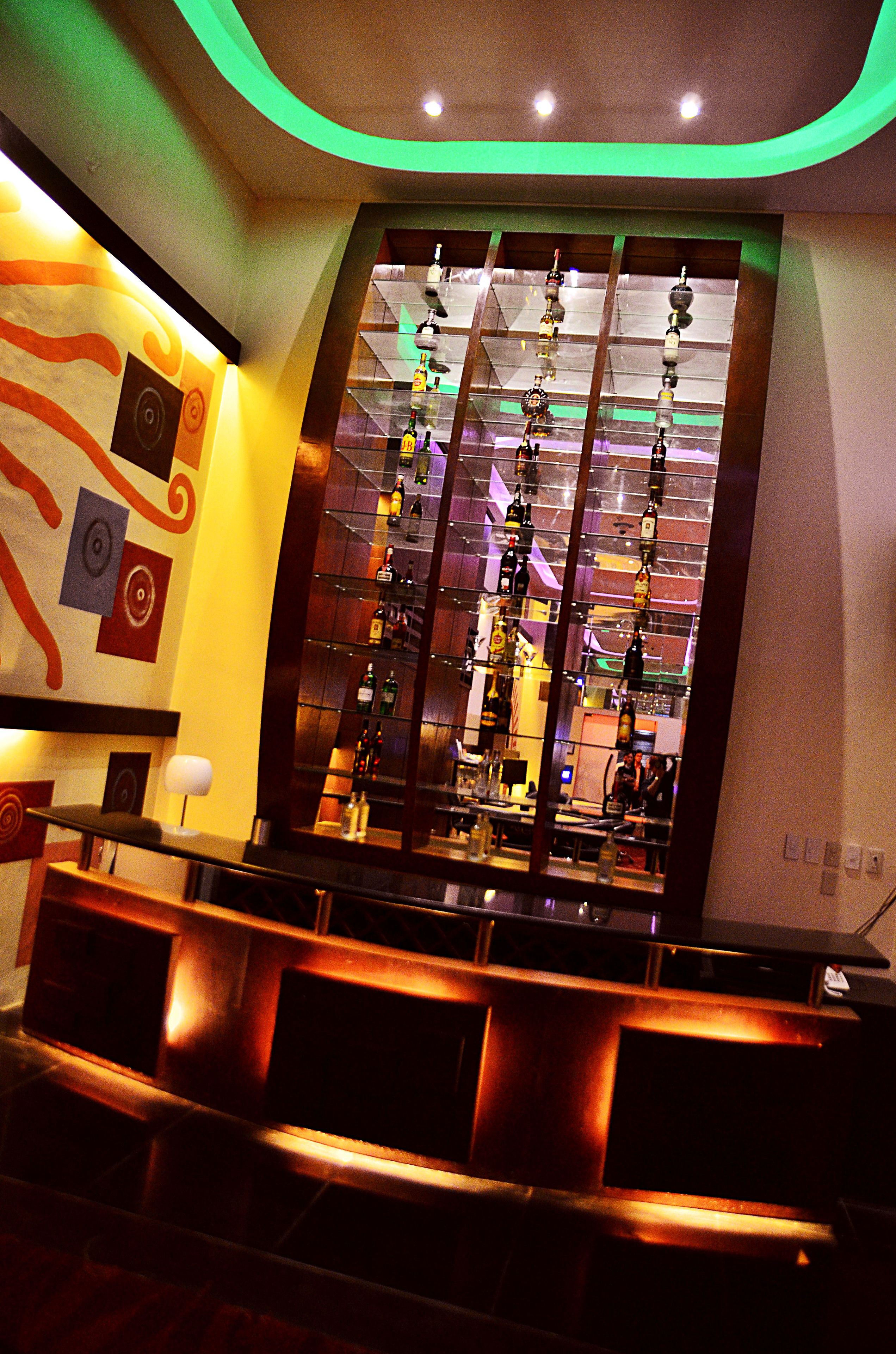 Eine Bar mit modernem Design, inklusive einer Glastrennwand mit hängenden Flaschen und einer Sitzecke mit gepolsterten Bänken.
