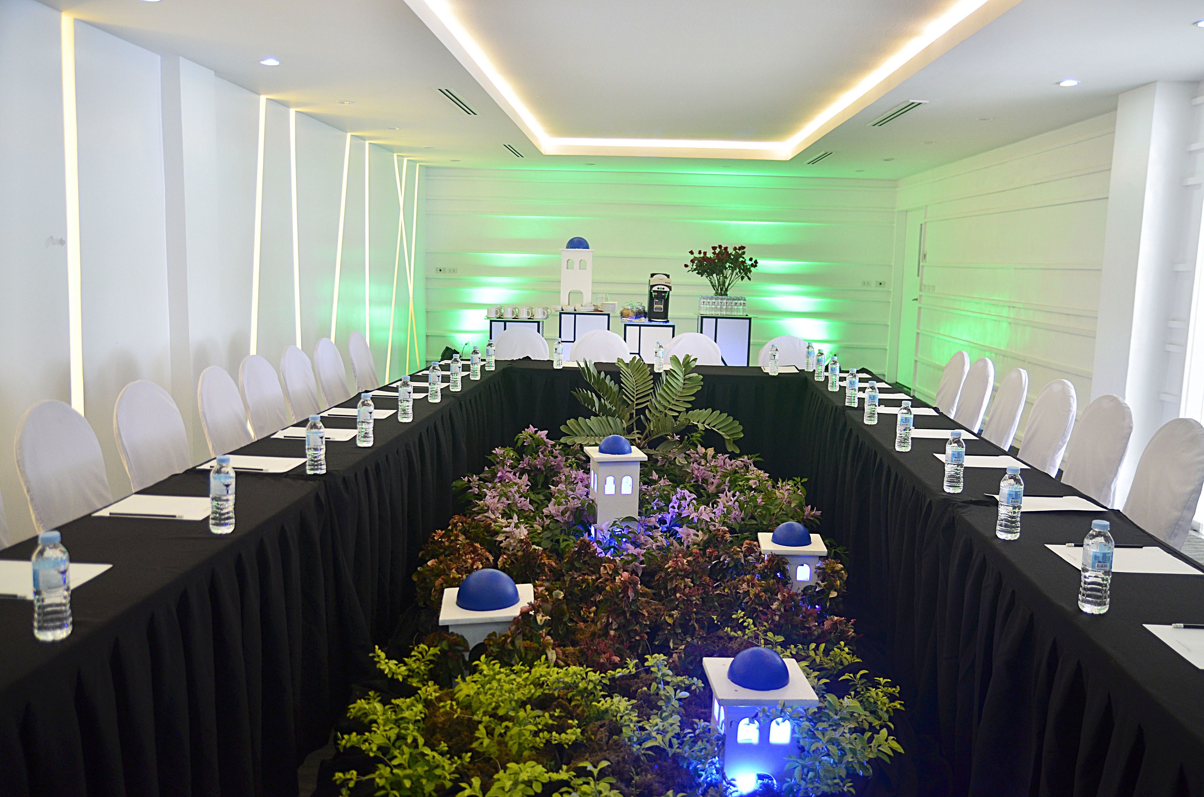 A conference room with a long table, white chairs, water bottles, and a decorative centerpiece.