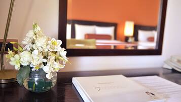 A hotel room with a bed, a bedside table with a book and papers, and a vase of flowers.