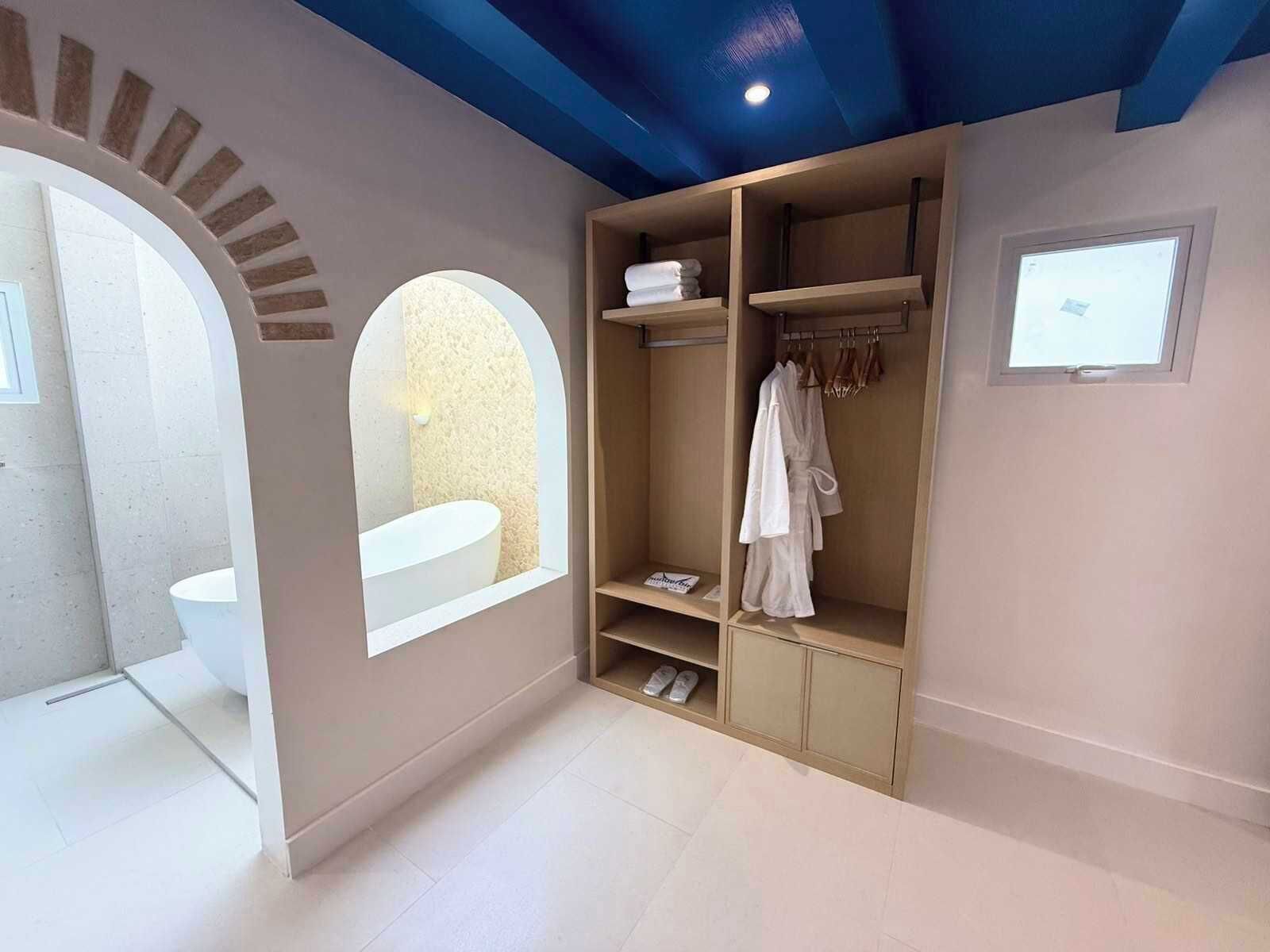 Baño con bañera, ducha y tocador. Se aprecia un tocador de madera con un espejo y un estante con toallas.