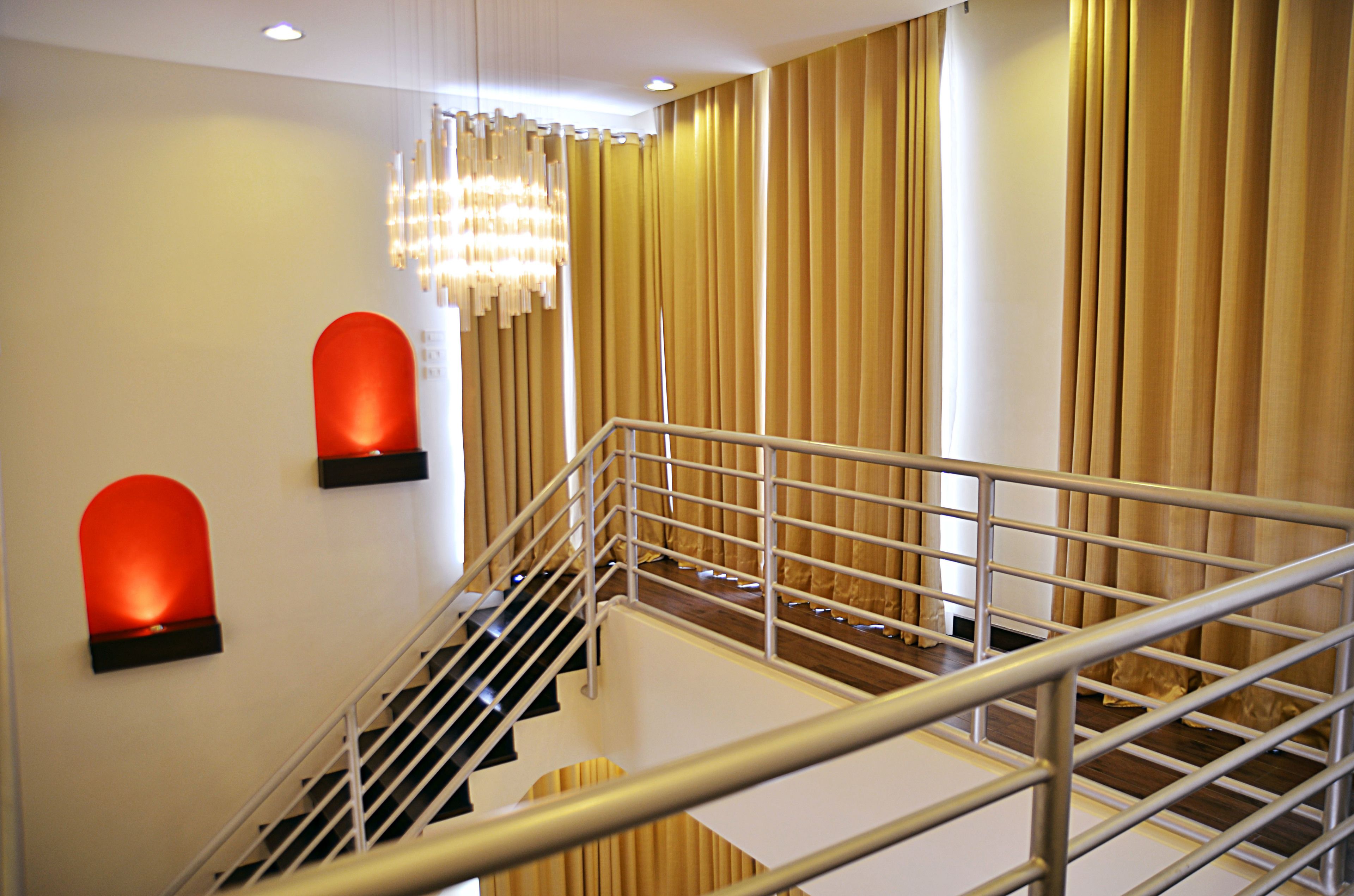 A staircase with metal railings, a chandelier, and curtains.