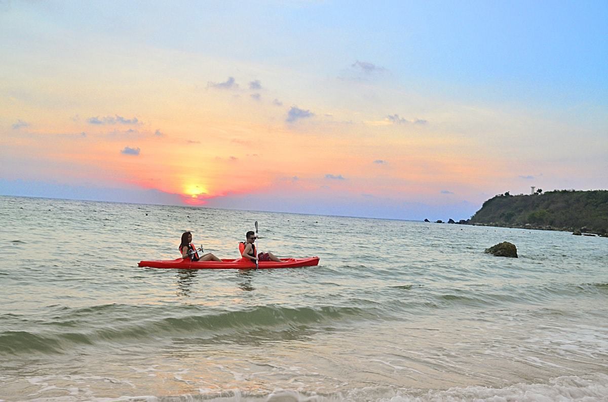 Two people kayaking on calm sea water during sunset.