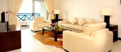 A modern living room with a sofa, coffee table, and lamps. There is a view of the outside through large windows.