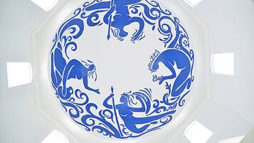 Una obra de arte circular azul en un techo blanco, con cuatro pequeñas ventanas a su alrededor.