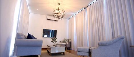 A modern living room with a chandelier, a flat-screen TV, and two grey sofas.