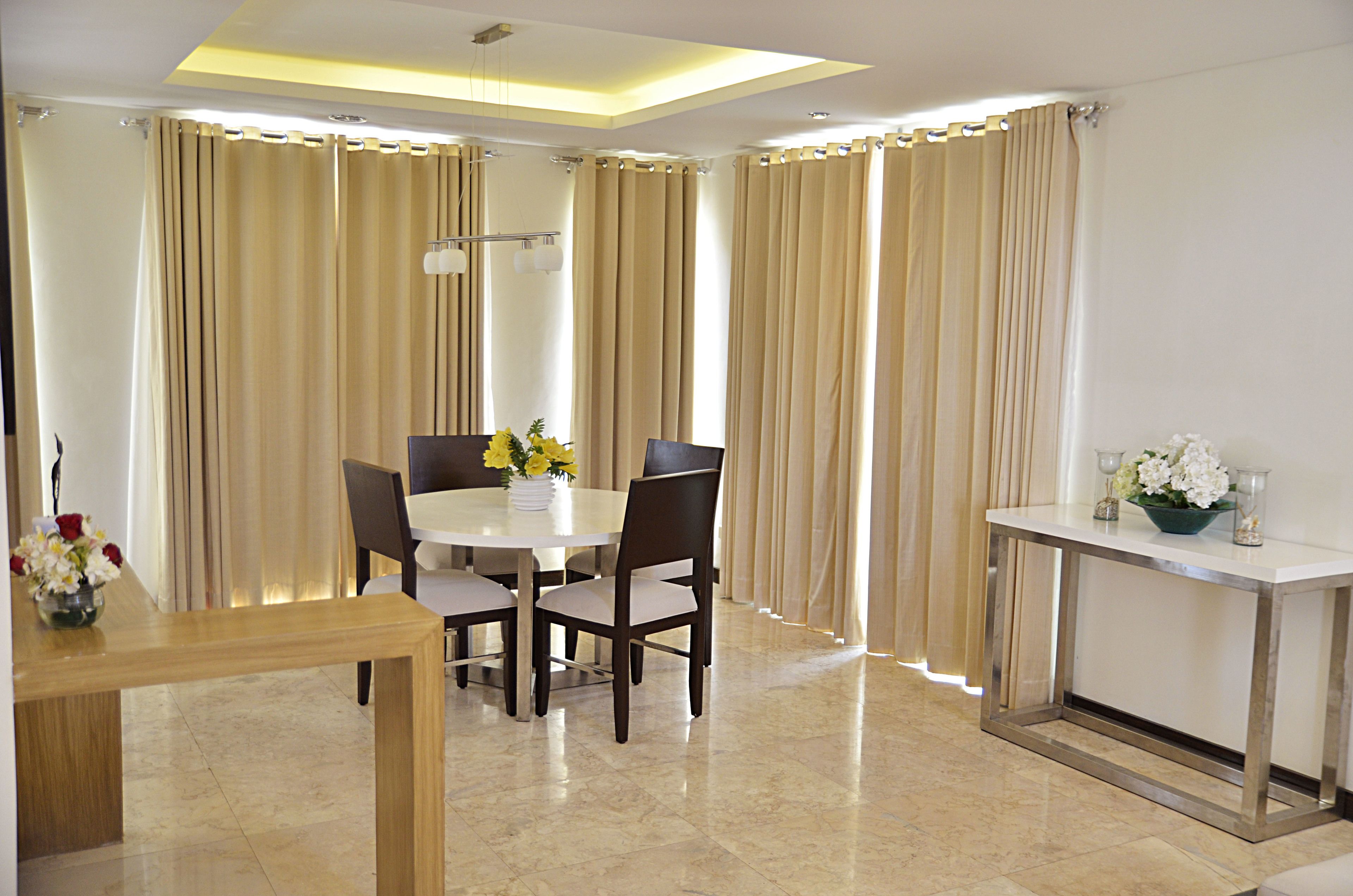 A dining area with a round table, four chairs, a vase with flowers, and a side table with a bowl of flowers.