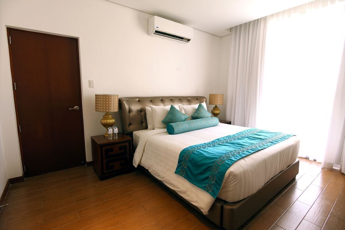 Une chambre avec un grand lit, une table de chevet avec des lampes, une porte en bois et un appareil de climatisation fixé au mur.
