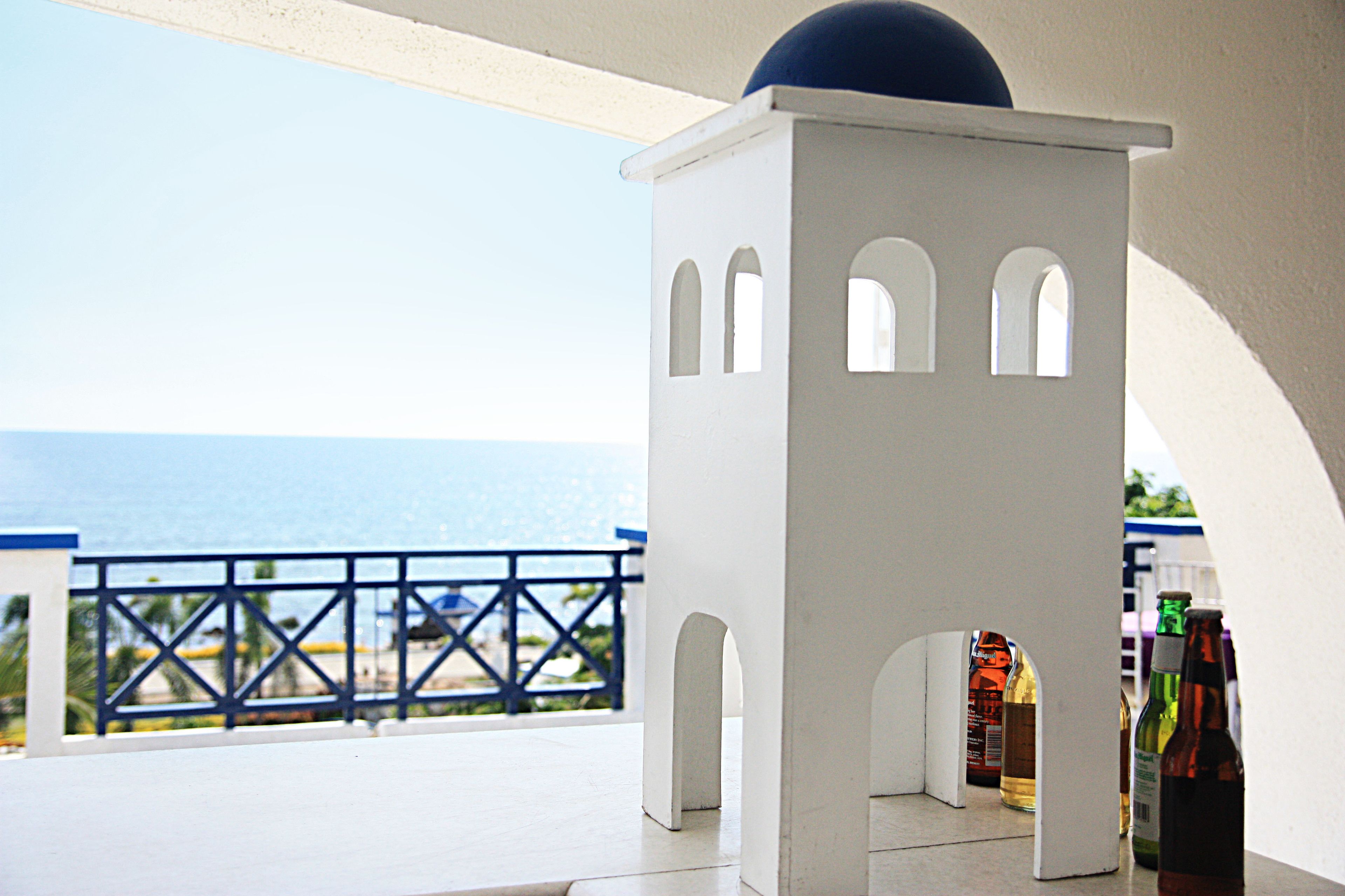 A white structure with arched openings, possibly a small kiosk or booth, on a balcony with a view of the sea.