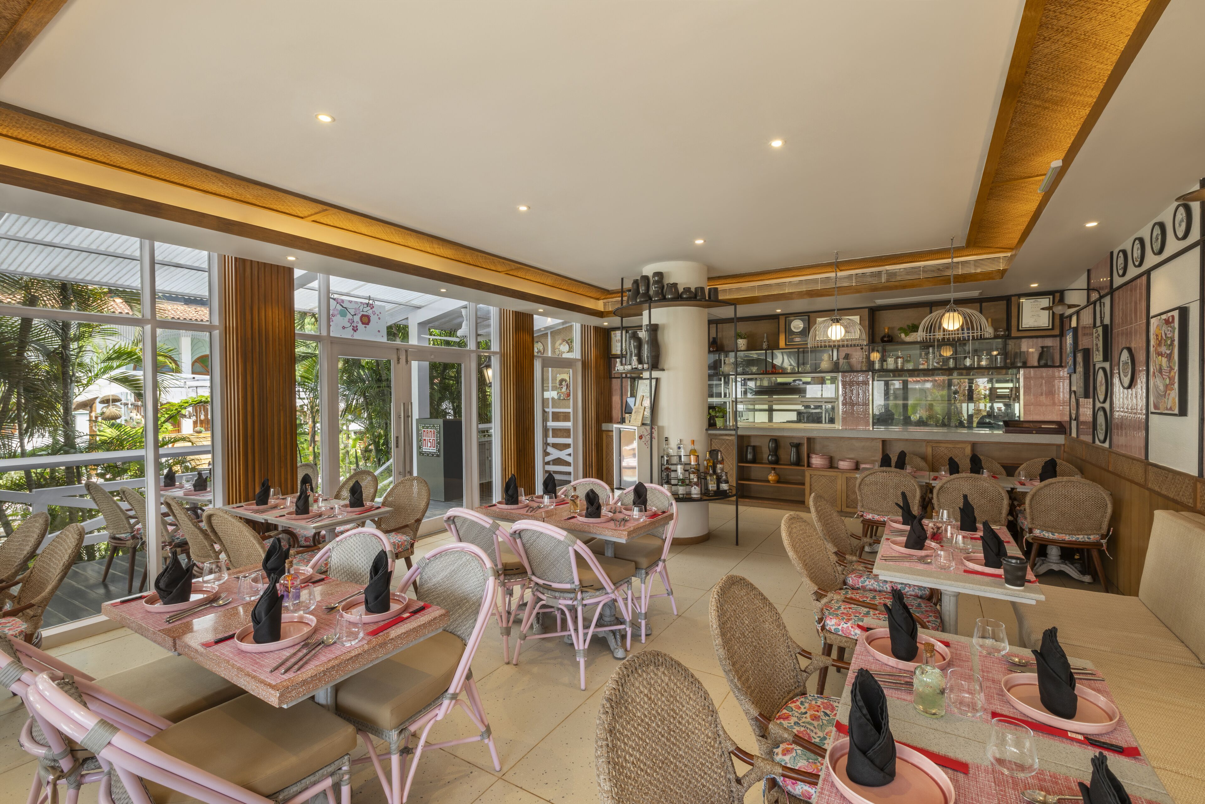 A restaurant with wicker chairs and tables, a bar area, and large windows offering a view of the outdoors.