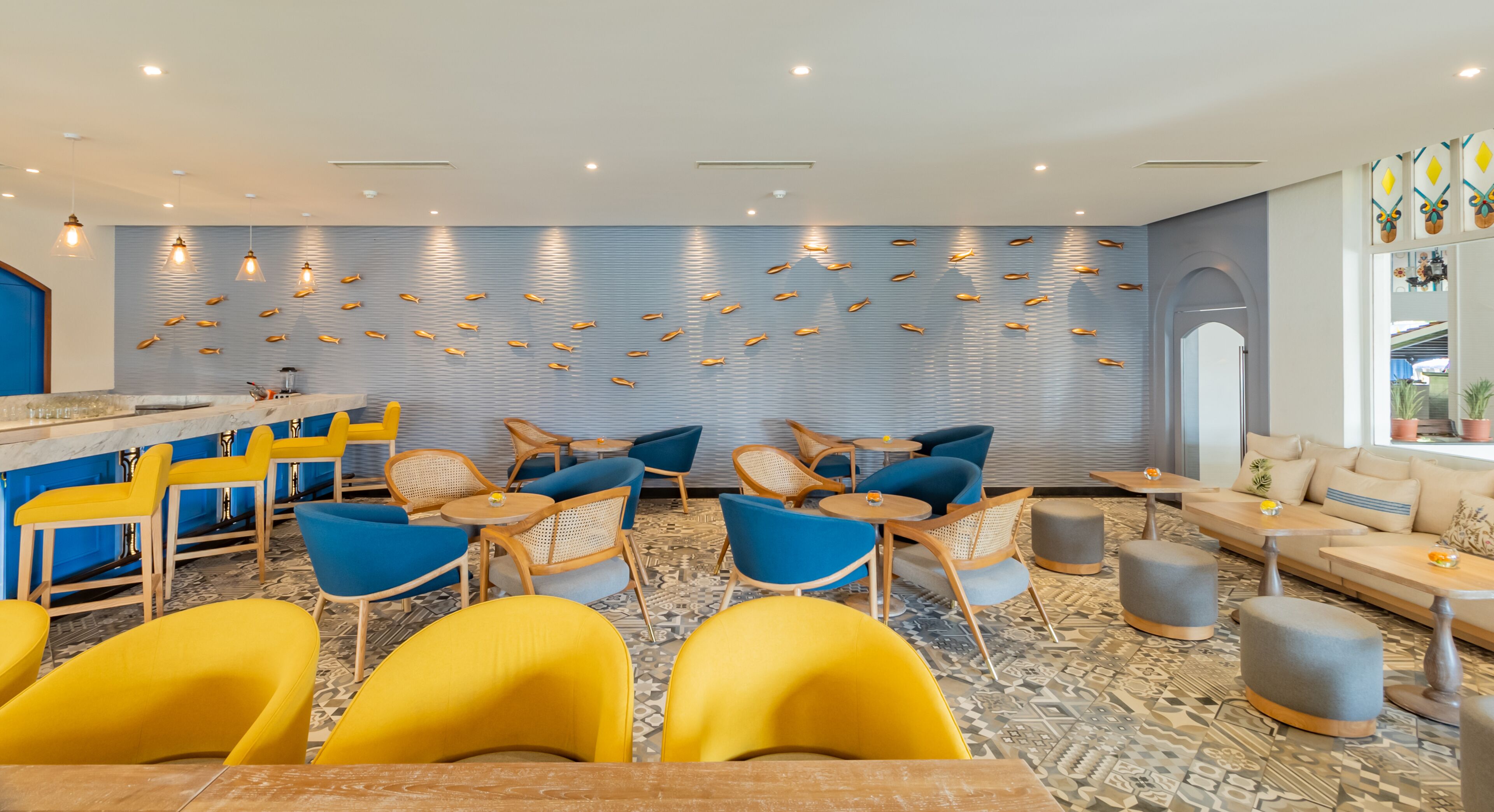 A modern lounge area with a bar, yellow and blue chairs, and a wall decorated with fish motifs.