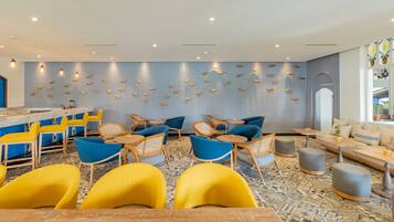 A modern lounge area with a bar, yellow and blue chairs, and a wall decorated with fish motifs.