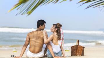 A couple sitting on a beach with a wicker basket and wine glasses.