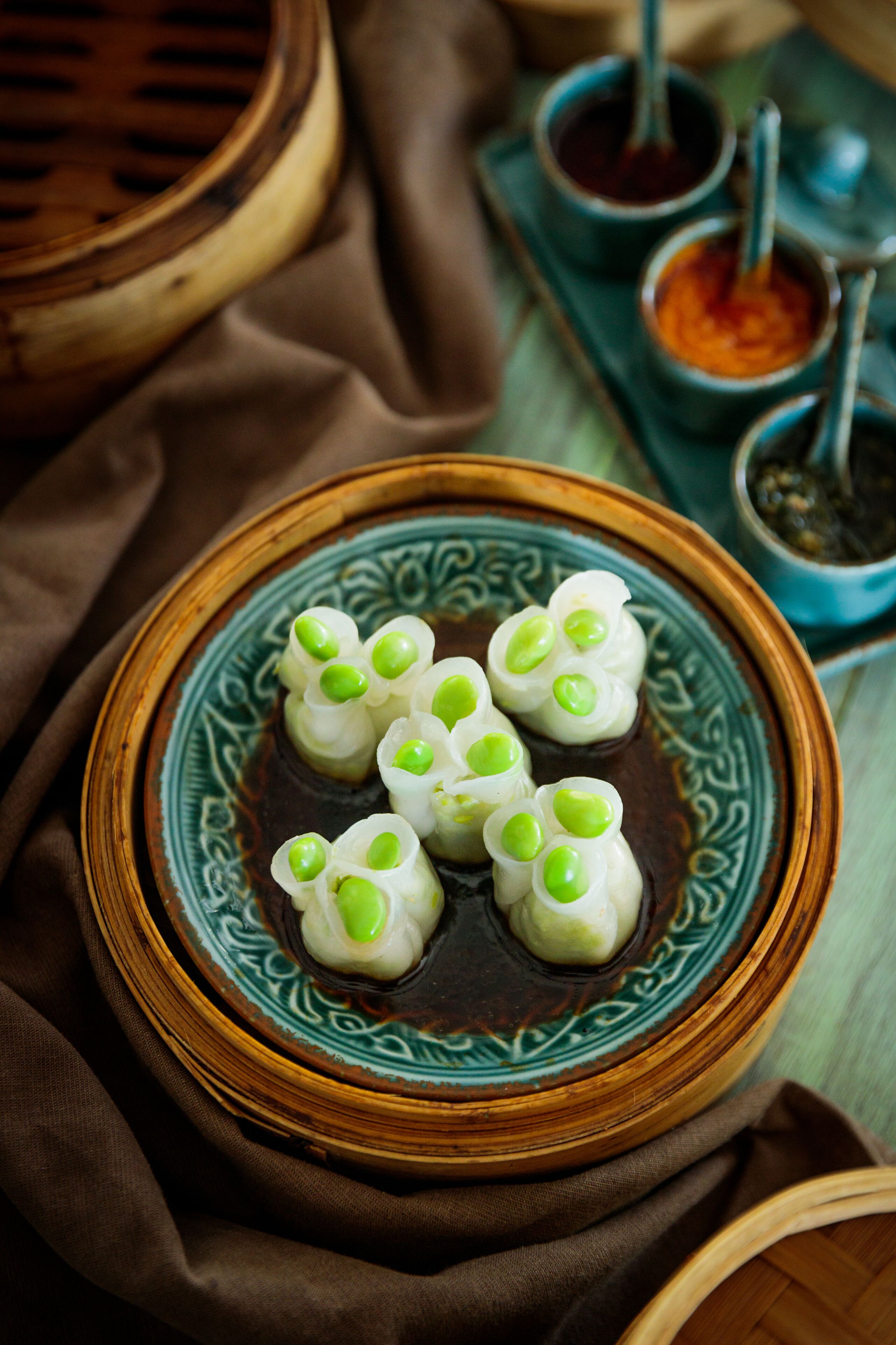 A plate of dumplings with green toppings, accompanied by dipping sauces in small bowls.