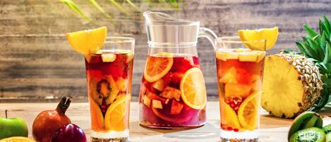 A wooden table with a pitcher and glasses of fruit-infused drinks, surrounded by fresh fruits and a pineapple.