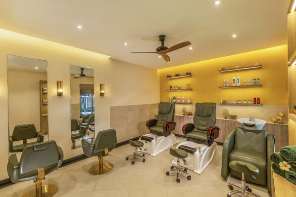 Un moderno cuarto de spa con tres sillones de masaje verdes, un ventilador de techo y estantes con diversos productos de spa.