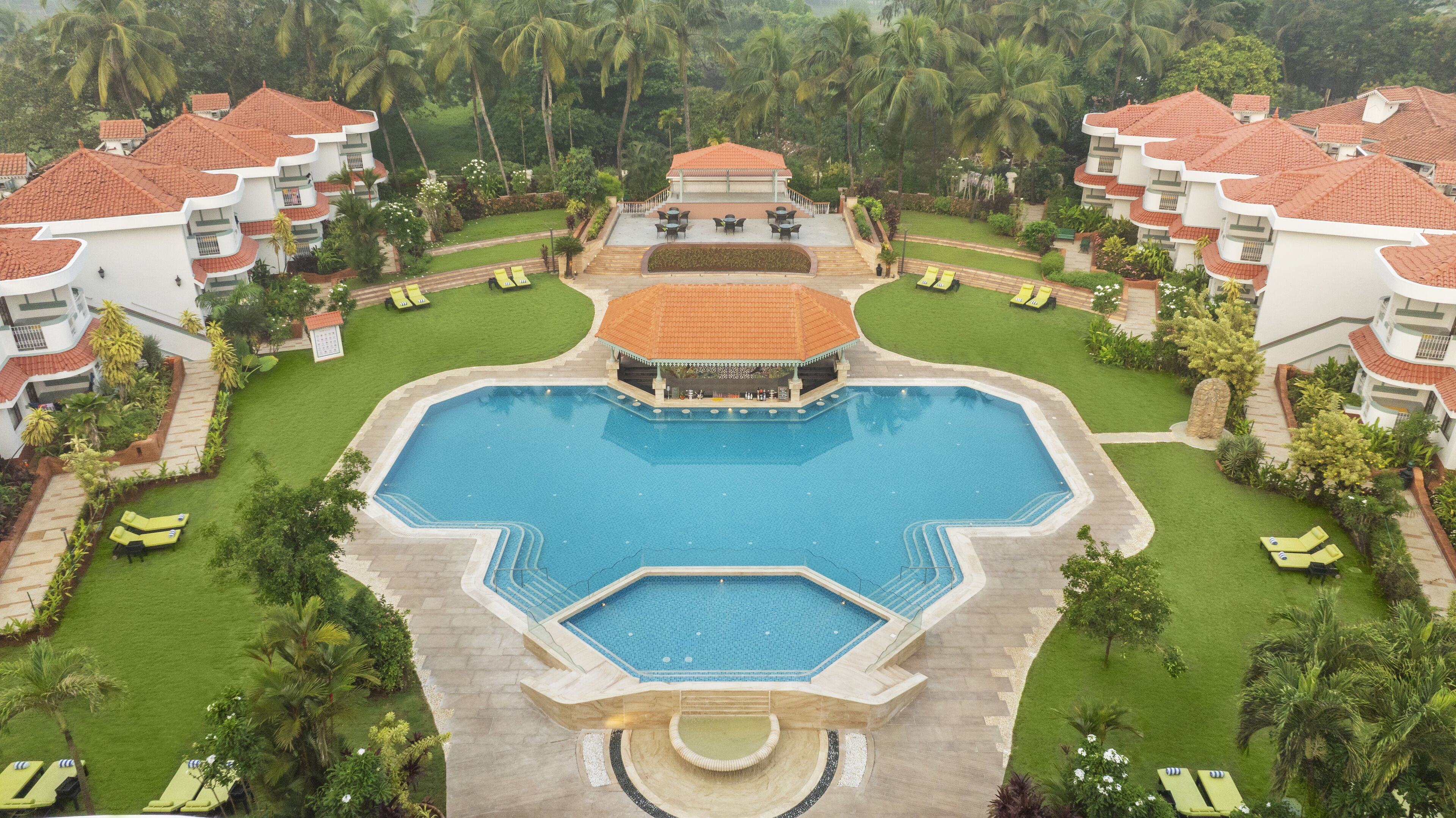 A resort with a central swimming pool, multiple lounge areas, and lush greenery.