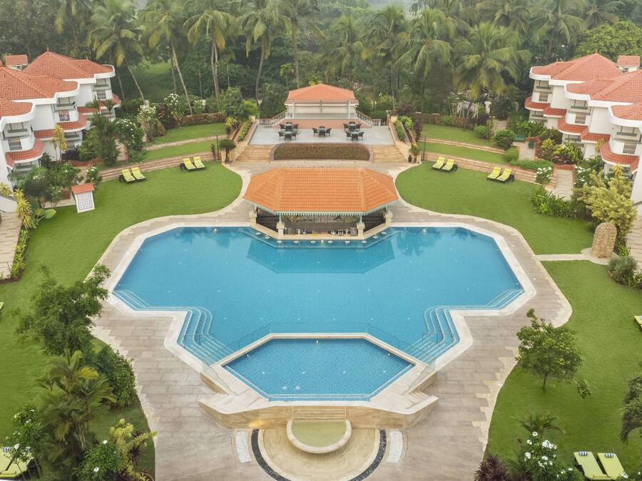 A resort with a central swimming pool, multiple lounge areas, and lush greenery.