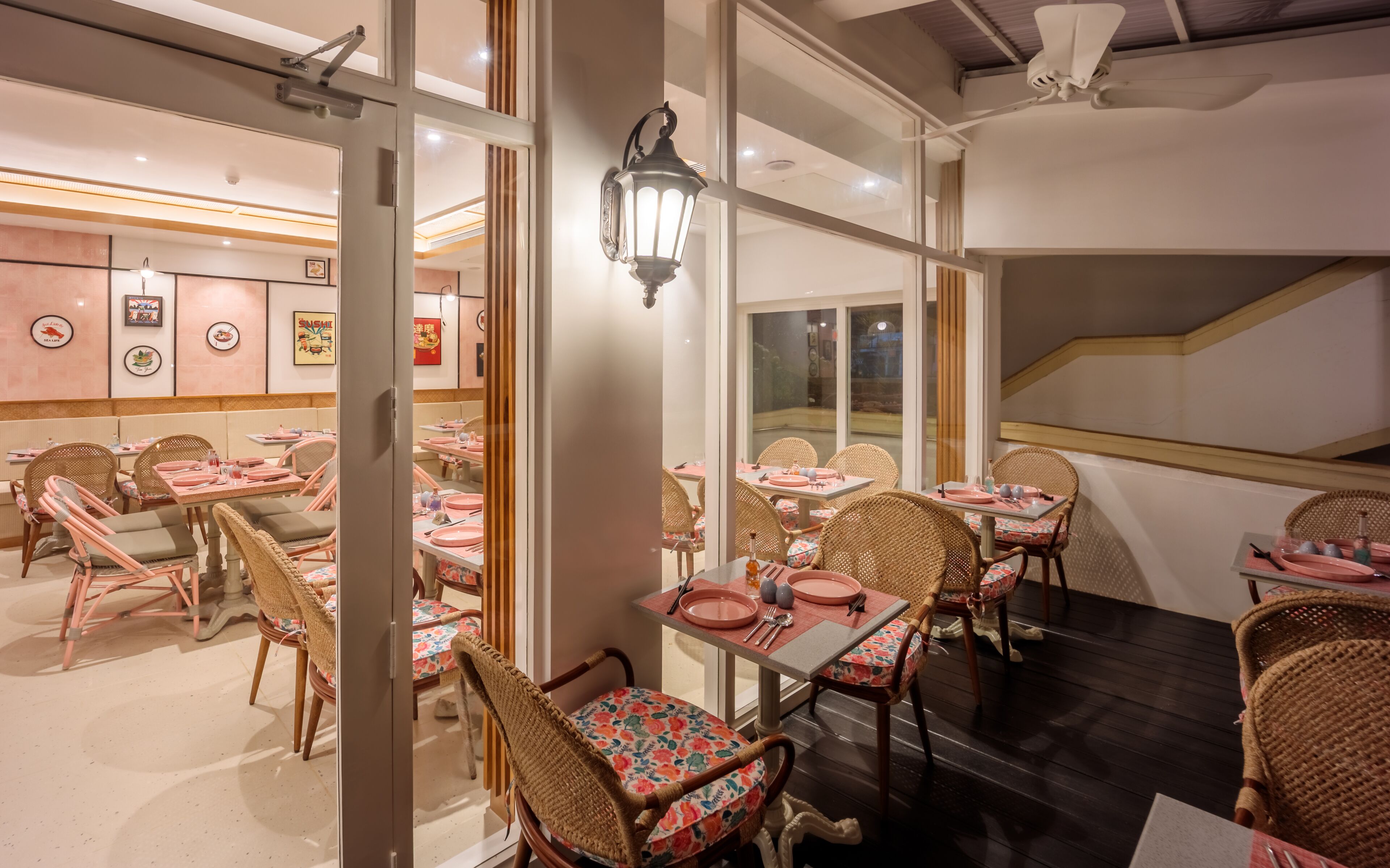Un restaurante con sillas y mesas de mimbre, una escalera y vistas al exterior.
