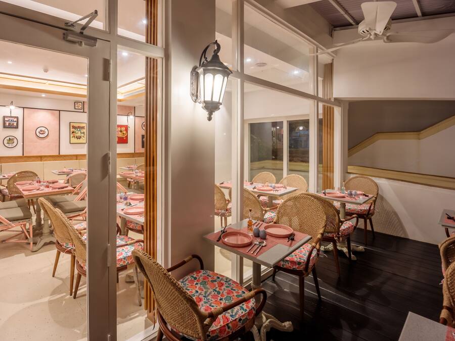 Un restaurante con sillas y mesas de mimbre, una escalera y vistas al exterior.