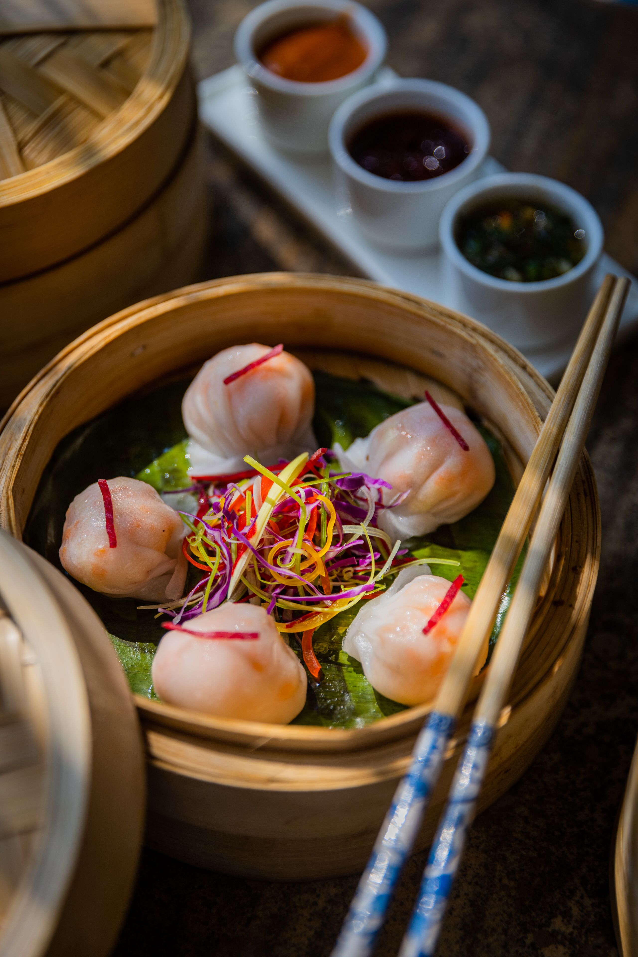 A bamboo steamer with dumplings and a pair of chopsticks.