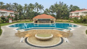 A swimming pool with a central water feature, surrounded by a paved area with lounge chairs. - Heritage Village Resort & Spa Goa (Cansaulim)