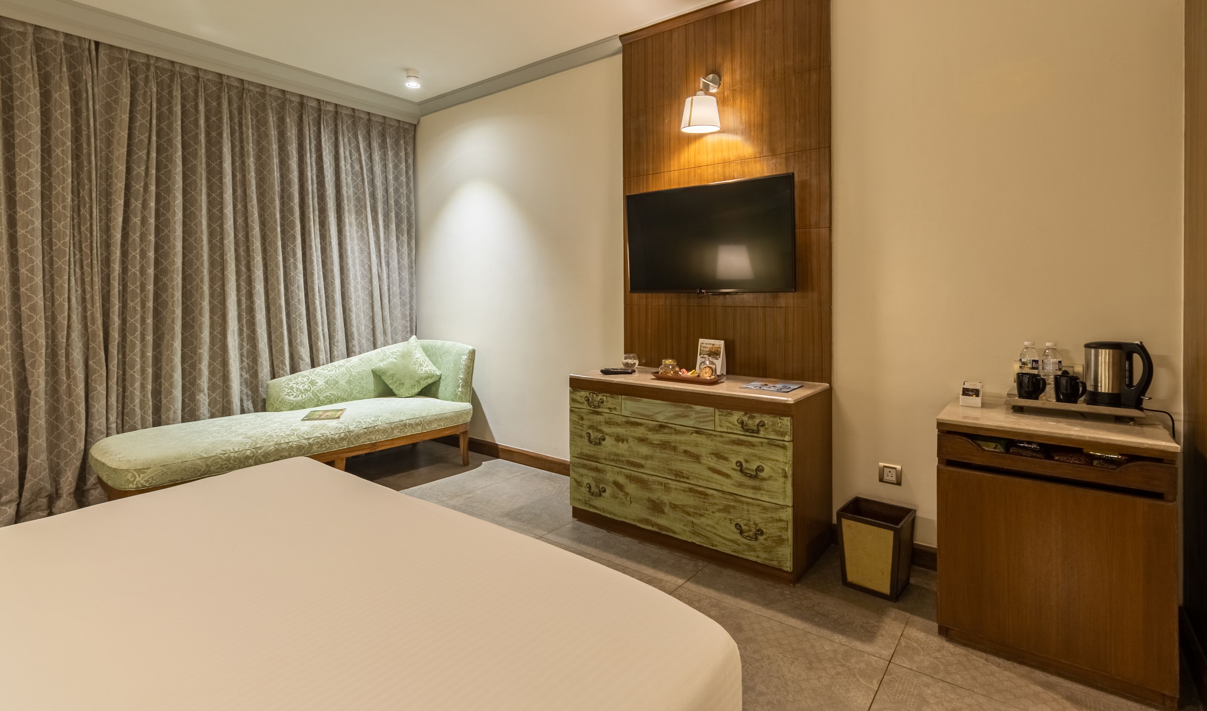 A hotel room with a large bed, a sofa, a TV mounted on the wall, a small wooden cabinet, and a coffee maker.
