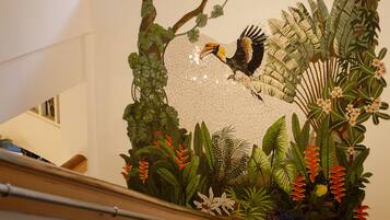 Una escalera con barandilla, un muro decorativo con motivos de aves y follaje, y una lámpara colgante.