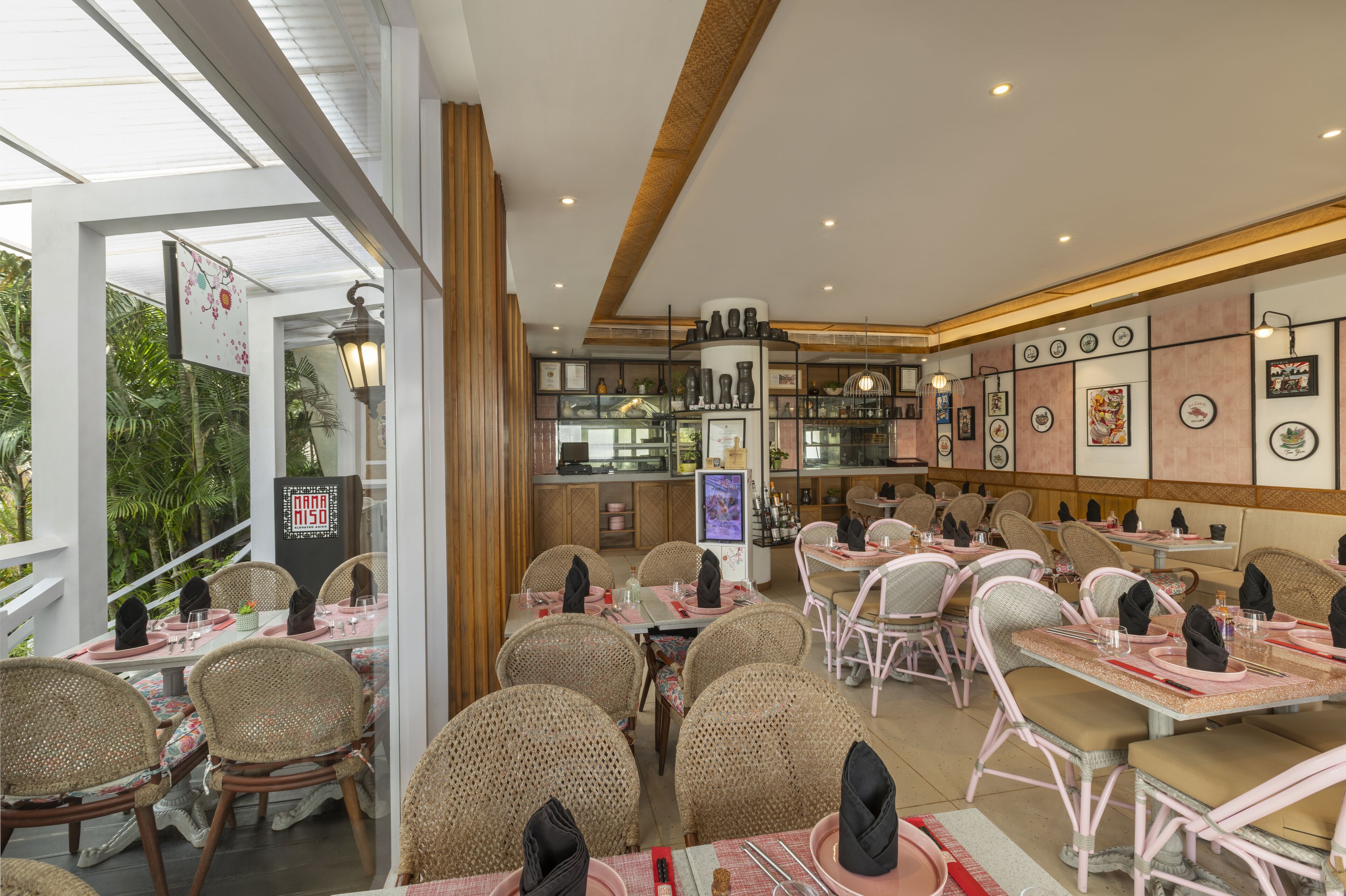 A restaurant with wicker chairs and tables, a bar area, and a view of greenery outside.